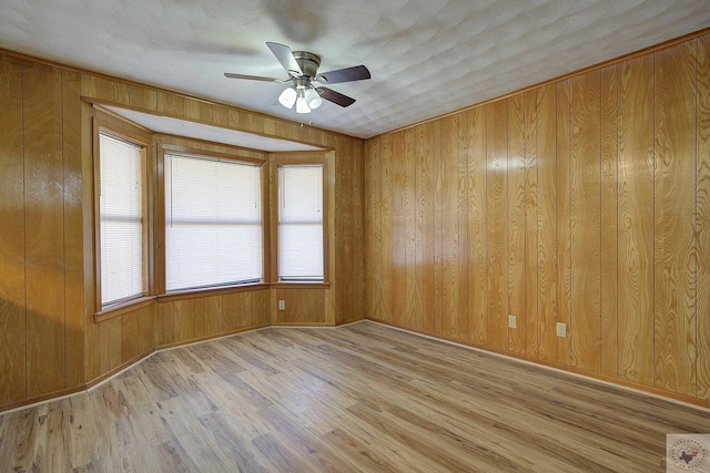 spare room with wooden walls, light wood-style floors, and ceiling fan