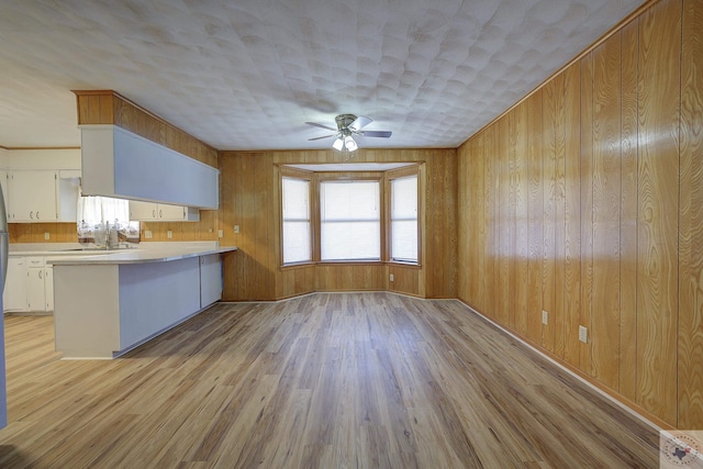 kitchen featuring light wood finished floors, ceiling fan, light countertops, a peninsula, and white cabinets