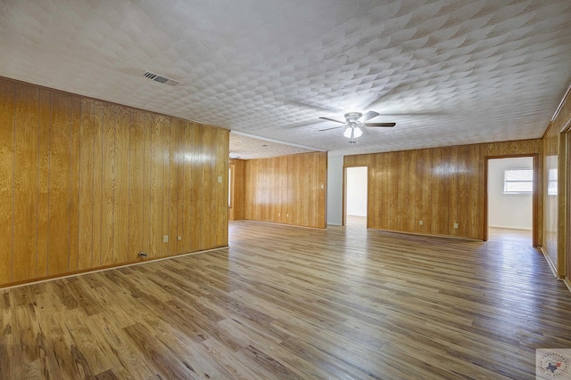 empty room featuring visible vents, a textured ceiling, wooden walls, and wood finished floors