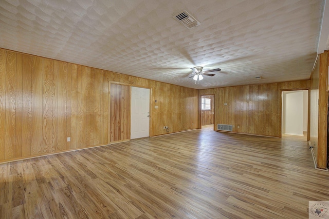 unfurnished room featuring visible vents, wooden walls, ceiling fan, and light wood finished floors