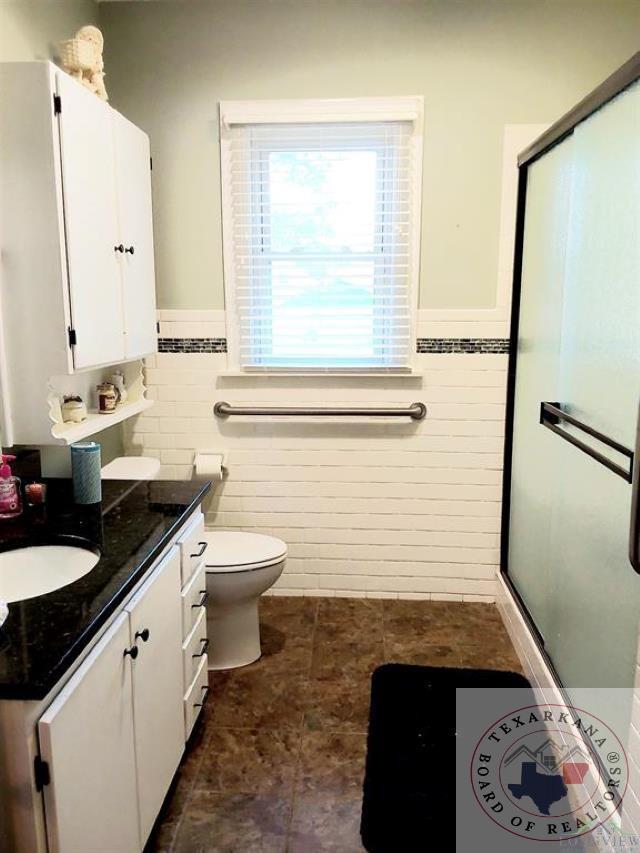 bathroom with toilet, a shower with shower door, vanity, and tile walls