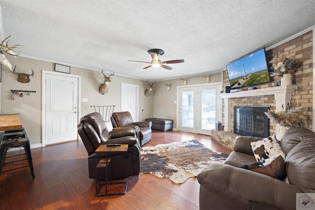 living area featuring a textured ceiling, a fireplace, wood finished floors, a ceiling fan, and ornamental molding