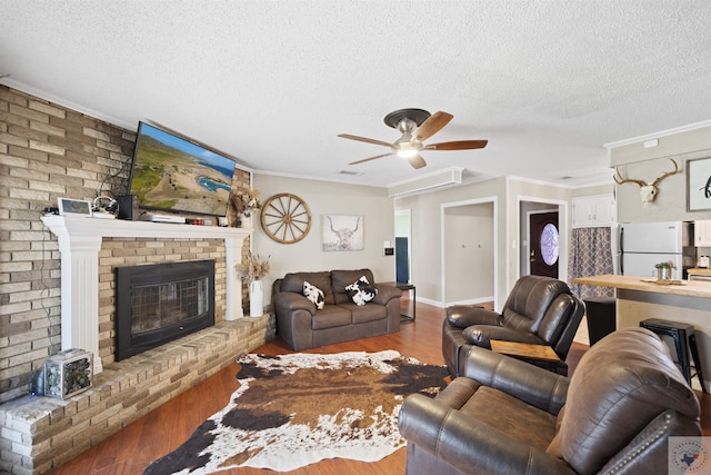 living area with a textured ceiling, ornamental molding, a fireplace, and wood finished floors