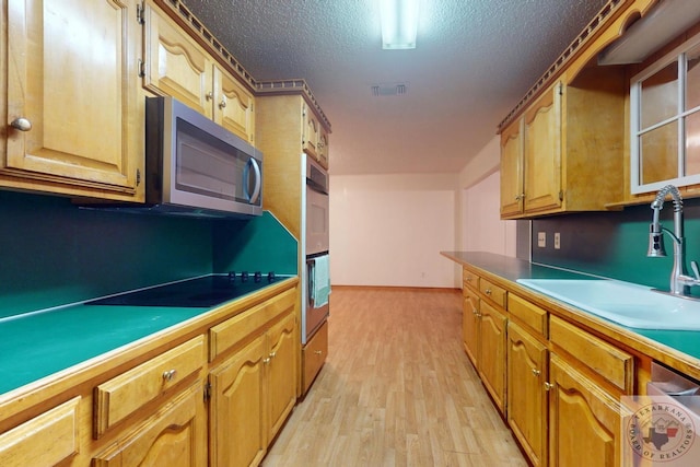 kitchen with sink, stainless steel appliances, light hardwood / wood-style floors, and a textured ceiling