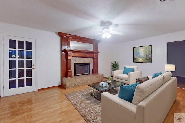 living room featuring ceiling fan, a high end fireplace, and light hardwood / wood-style floors