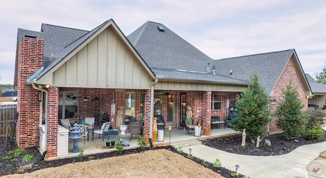 back of property featuring a shingled roof, a patio area, brick siding, and board and batten siding