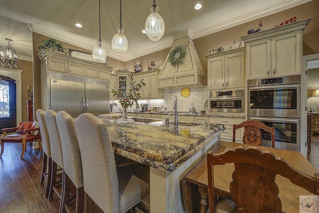 kitchen with appliances with stainless steel finishes, cream cabinets, glass insert cabinets, and decorative light fixtures