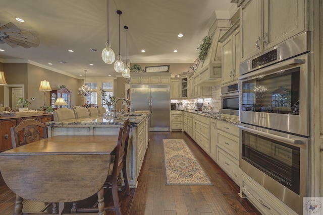 kitchen featuring glass insert cabinets, a kitchen island with sink, appliances with stainless steel finishes, and cream cabinets