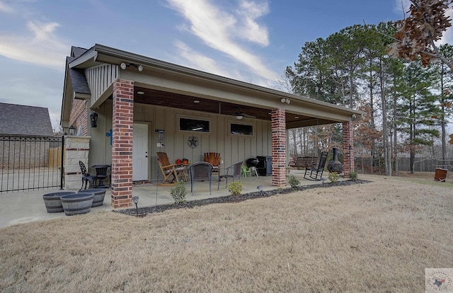 view of front of property with brick siding, fence, a front yard, board and batten siding, and a patio area