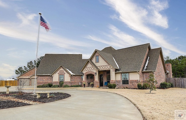 view of front of home featuring a shingled roof, concrete driveway, brick siding, and fence