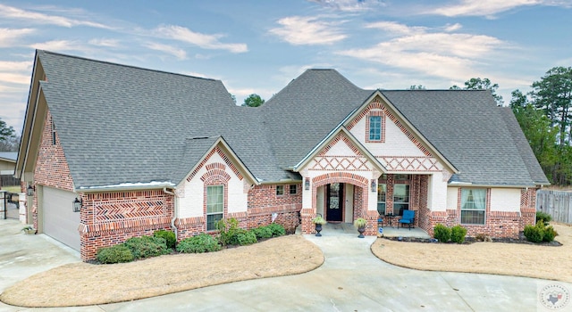 tudor-style house featuring driveway, a garage, a shingled roof, covered porch, and brick siding