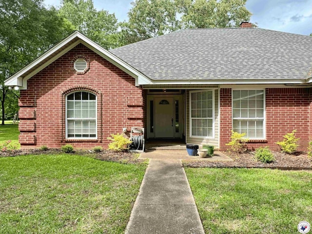 ranch-style house with a chimney, brick siding, a front lawn, and a shingled roof