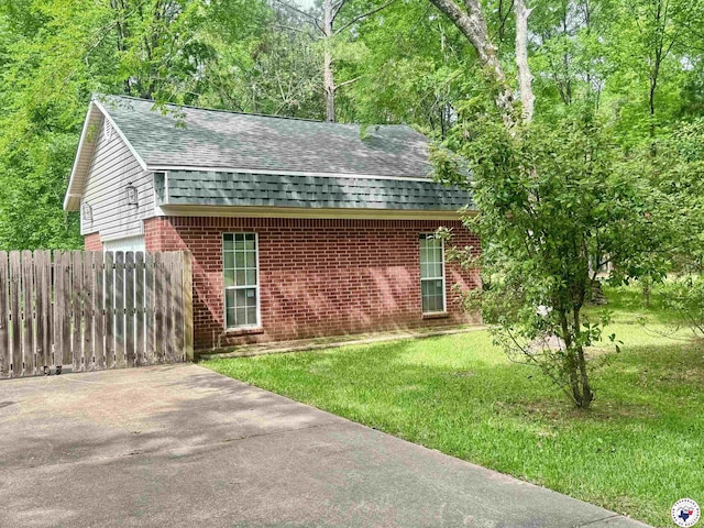 exterior space featuring fence, a yard, a shingled roof, and brick siding