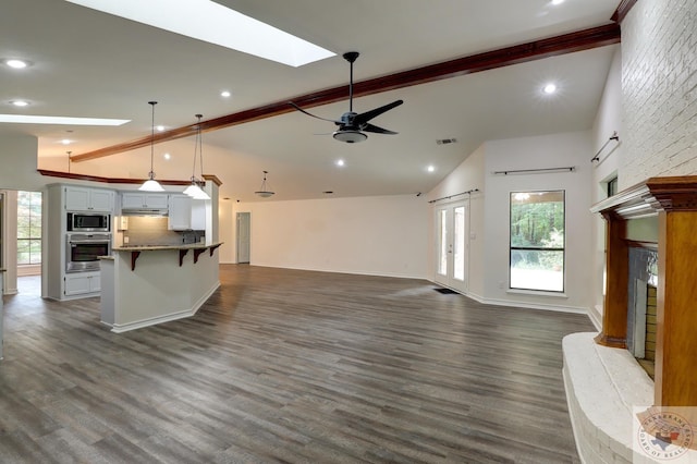 unfurnished living room featuring a fireplace, ceiling fan, beam ceiling, and a skylight