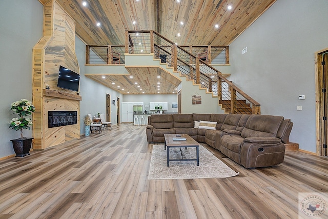 living room with wood-type flooring, a towering ceiling, and a large fireplace