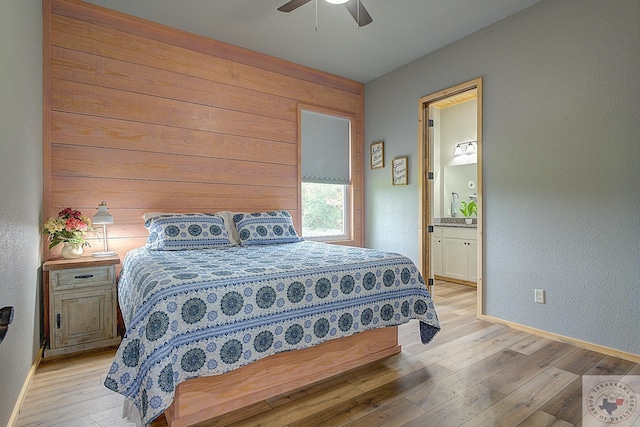 bedroom with ceiling fan, wooden walls, light hardwood / wood-style floors, and ensuite bath