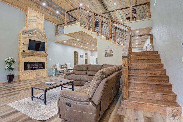 living room with wood-type flooring, a high ceiling, a large fireplace, and beam ceiling