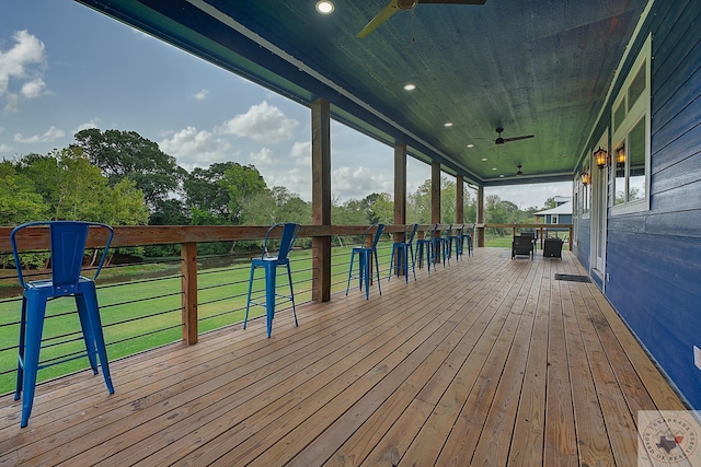 wooden terrace featuring ceiling fan, an outdoor bar, and a lawn