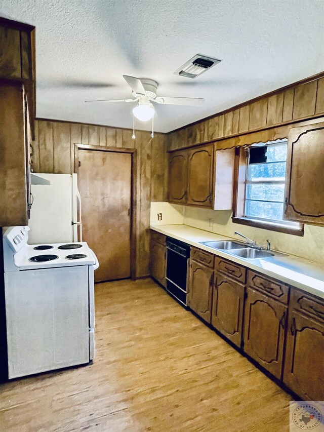 kitchen featuring white appliances, a textured ceiling, wooden walls, sink, and light wood-type flooring