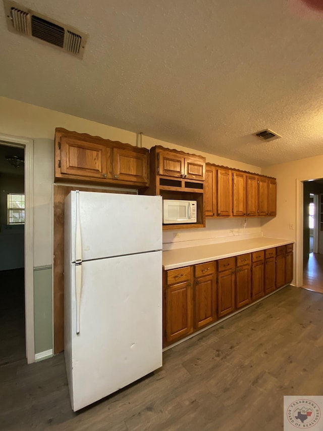 kitchen featuring dark wood-type flooring, white appliances, and a textured ceiling