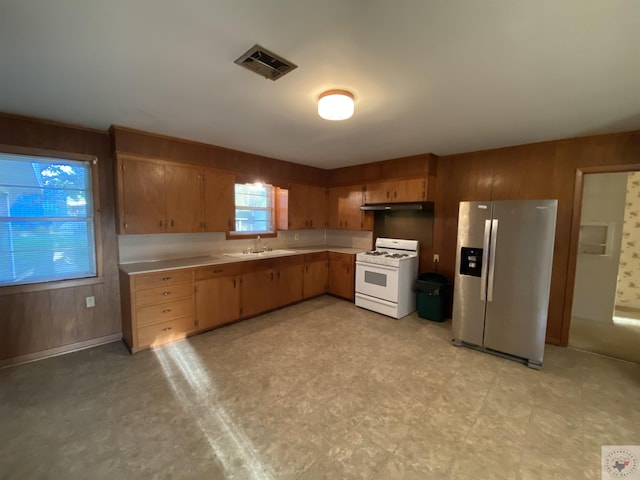 kitchen featuring white range with gas stovetop, wood walls, sink, and stainless steel fridge