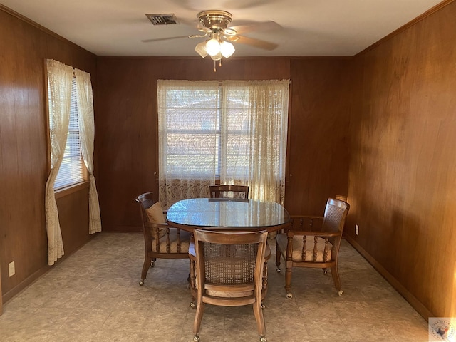 dining space with crown molding, wooden walls, and ceiling fan