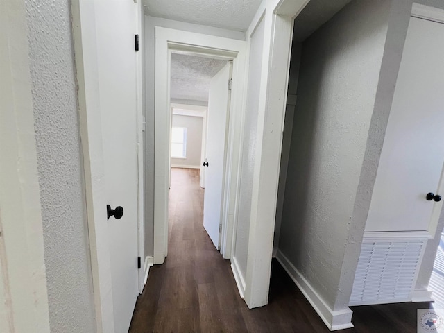 corridor with dark hardwood / wood-style flooring and a textured ceiling