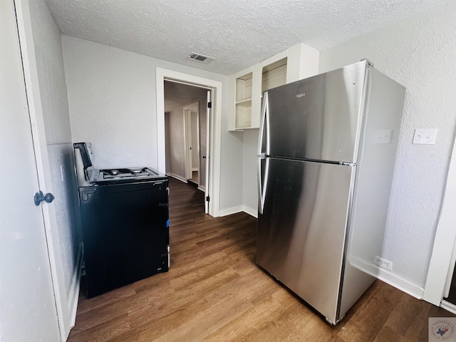 kitchen with black range with gas cooktop, stainless steel refrigerator, a textured ceiling, and wood-type flooring