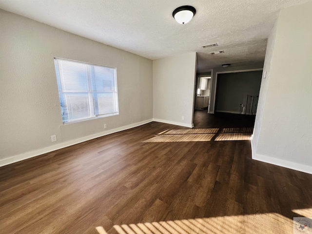 spare room featuring a textured ceiling and dark hardwood / wood-style flooring