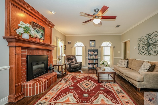 living room with visible vents, a brick fireplace, crown molding, wood finished floors, and a ceiling fan