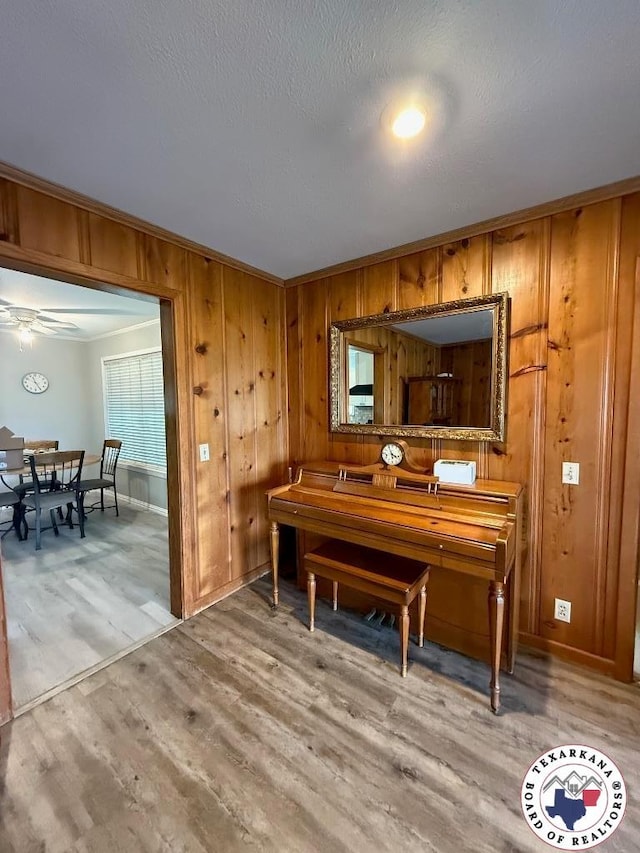 184 E Elliott Ln, Dekalb, TX 75559 - living area featuring light wood-style flooring, wood walls, ornamental molding, a ceiling fan, and baseboards