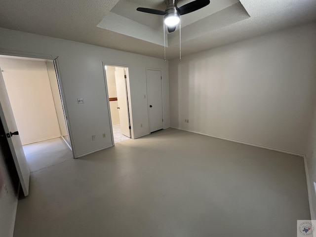 unfurnished bedroom with ceiling fan, connected bathroom, a textured ceiling, and a tray ceiling