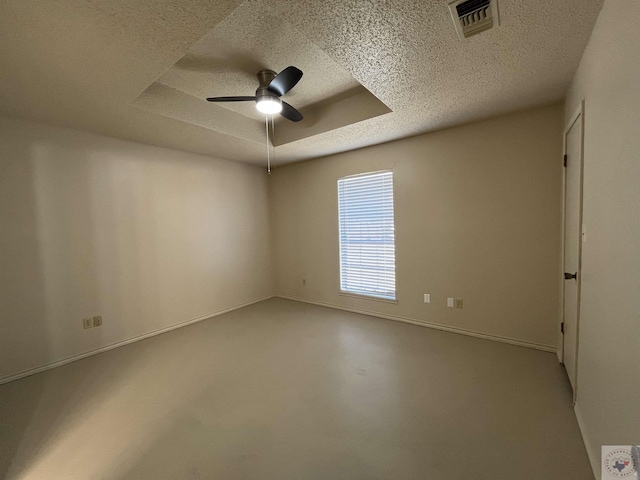 empty room featuring ceiling fan, concrete floors, a raised ceiling, and a textured ceiling