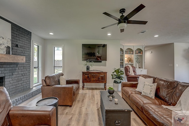 living room with built in features, ceiling fan, light hardwood / wood-style floors, and a fireplace