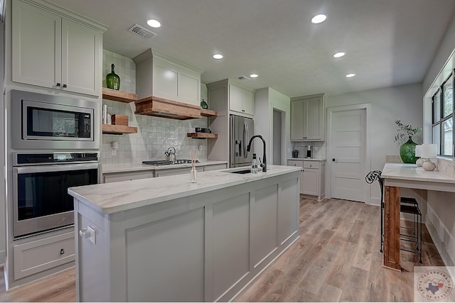 kitchen with stainless steel appliances, tasteful backsplash, light hardwood / wood-style floors, sink, and a center island with sink