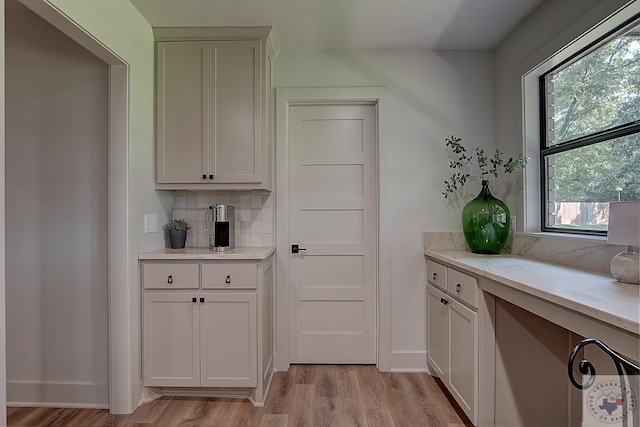 interior space with backsplash, white cabinetry, light stone countertops, and light hardwood / wood-style floors