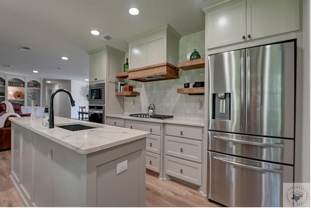 kitchen featuring appliances with stainless steel finishes, tasteful backsplash, sink, light stone counters, and a center island with sink