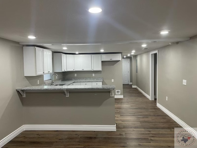 kitchen with white cabinets, sink, kitchen peninsula, dark hardwood / wood-style flooring, and light stone counters