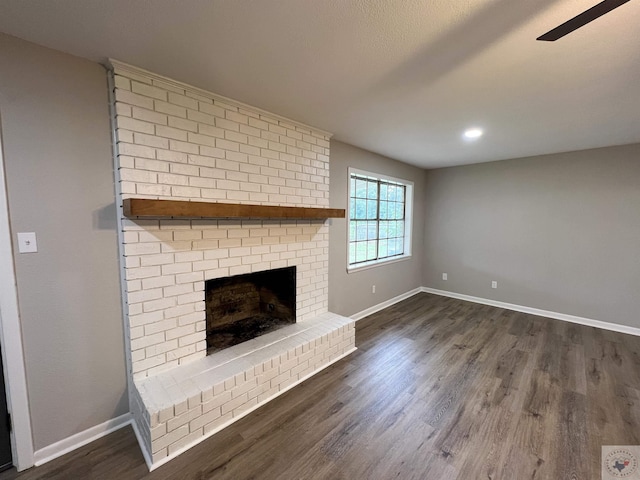 unfurnished living room featuring a brick fireplace and dark wood-type flooring