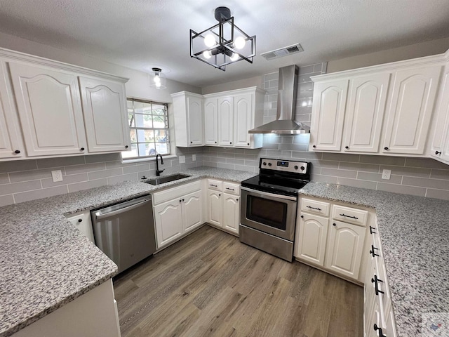 kitchen featuring sink, white cabinets, stainless steel appliances, light stone countertops, and wall chimney exhaust hood