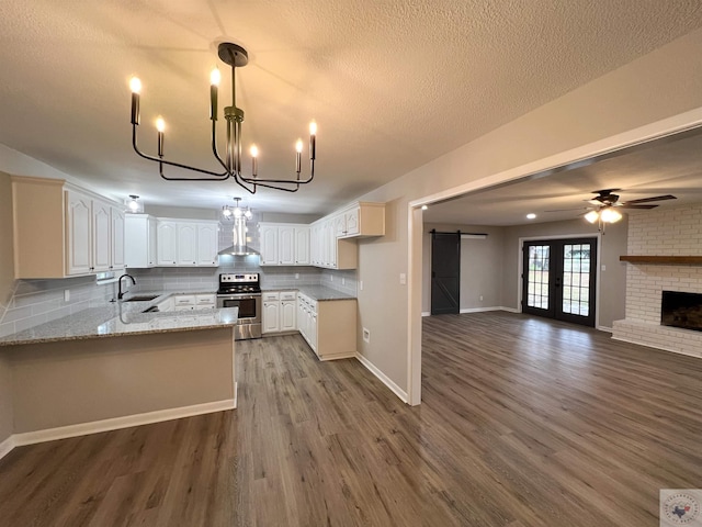 kitchen featuring stainless steel electric range oven, sink, hanging light fixtures, kitchen peninsula, and a barn door