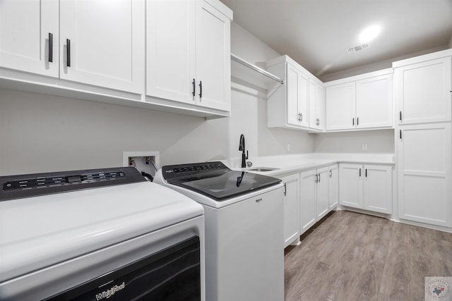 clothes washing area with cabinet space, visible vents, light wood-style floors, a sink, and independent washer and dryer