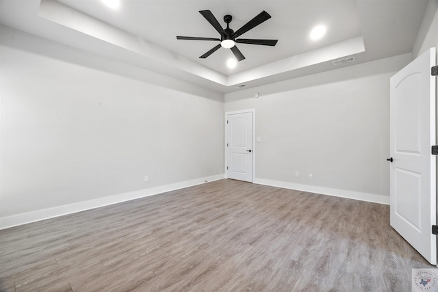 spare room featuring a raised ceiling, baseboards, visible vents, and light wood finished floors