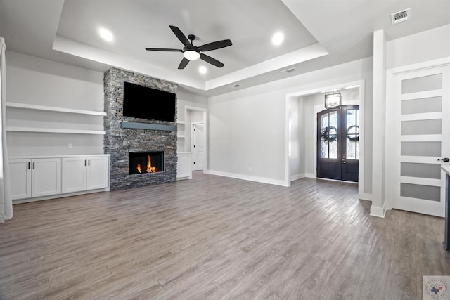 unfurnished living room with visible vents, built in features, a tray ceiling, french doors, and light wood-style floors