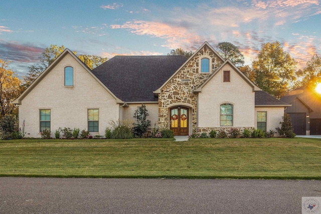 view of front of property with brick siding, stone siding, roof with shingles, french doors, and a front yard