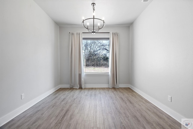 unfurnished room with a chandelier, light wood-style flooring, and baseboards