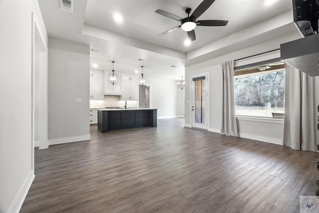 unfurnished living room with dark wood-style floors, visible vents, and a raised ceiling