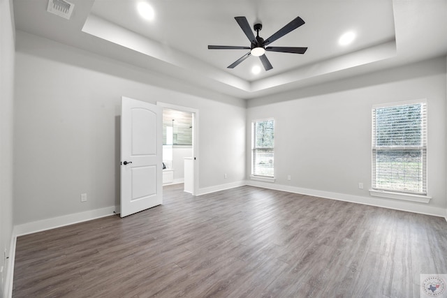 unfurnished room featuring visible vents, dark wood finished floors, baseboards, ceiling fan, and a tray ceiling