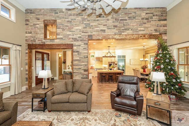 living room with hardwood / wood-style flooring, a towering ceiling, crown molding, and ceiling fan with notable chandelier