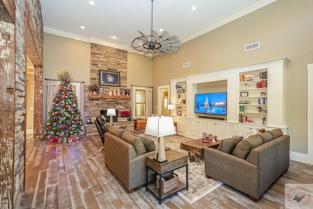 living room with a towering ceiling, ornamental molding, a fireplace, and light wood-type flooring